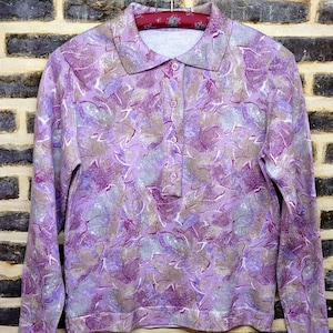 Peut inclure: Une chemise à manches longues de couleur violette avec un motif floral. La chemise a un col et une fermeture boutonnée.