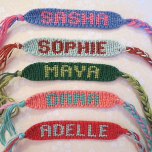 May include: Five colorful friendship bracelets with the names Sasha, Sophie, Maya, Dana, and Adella woven into them.