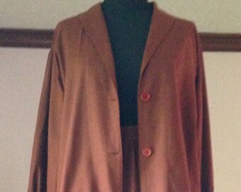 Può includere: Un completo vintage a due pezzi in una tonalità marrone rossiccio tenue. Il completo presenta una giacca a maniche lunghe con due bottoni e una gonna abbinata al ginocchio. L'outfit è esposto su un manichino.