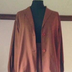 Op de afbeelding: Een vintage tweedelig pak in een gedempte roodbruine tint. Het pak heeft een blazer met lange mouwen en twee knopen en een bijpassende knielange rok. De outfit wordt op een mannequin gepresenteerd.