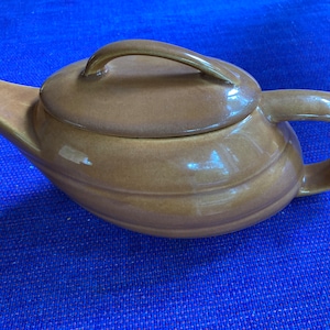 May include: A brown ceramic teapot with a lid and handle. The teapot has a curved spout and a rounded body with horizontal ridges. The handle is arched, and the lid has a small handle. The teapot is on a blue surface.