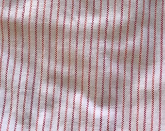 May include: Close-up of a white fabric with a repeating pattern of thin, vertical red stripes. The stripes are evenly spaced and create a textured appearance. The fabric appears to be a woven material.