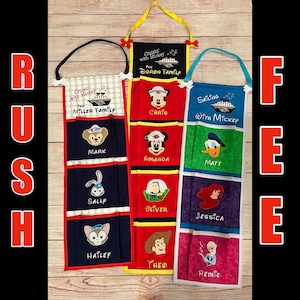 May include: A set of six colorful fabric storage pockets with embroidered Disney characters and names. Each pocket has a different theme, including "Cruisin' with Mickey", "Sailing with Mickey", and "The Duron Family".