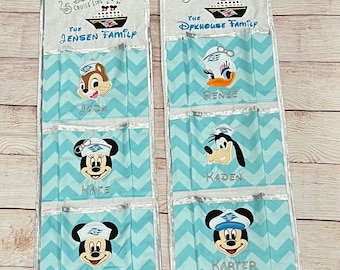 May include: Two blue and white fabric hanging organizers with Disney Cruise Line logos and character embroidery. The organizers have pockets for each family member: Judy, Kate, Joe, Evp, Renee, Kaden, Karter, and Rolin.