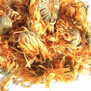 Puede incluir: Primer plano de flores de caléndula secas, que muestran pétalos de color naranja y amarillo vibrantes. La imagen destaca la textura y los detalles de los pétalos y los capullos, con un enfoque en la apariencia natural y orgánica del producto herbal.