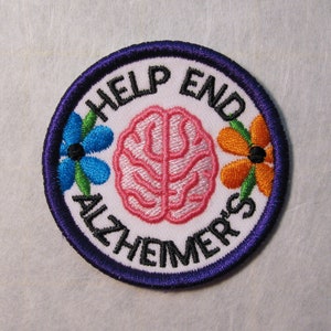 May include: White embroidered patch with a purple border. The patch features a pink brain, two flowers, and the text "Help End Alzheimer's".