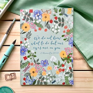 Könnte beinhalten: Eine hellblaue Karte mit einem Blumenmuster und dem Zitat "Wir wissen nicht, was wir tun sollen, aber unsere Augen sind auf dich gerichtet." mit dem Bibelvers "2 Chroniken 20,12".