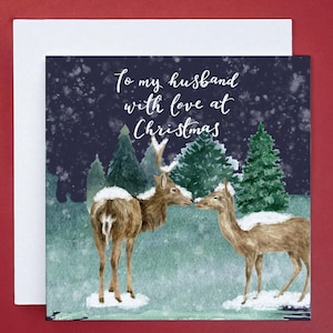 Könnte beinhalten: Weihnachtskarte mit einer Aquarellillustration von zwei Hirschen in einem verschneiten Wald. Auf der Karte steht "To my husband with love at Christmas". Der Hintergrund ist dunkelblau mit fallendem Schnee.