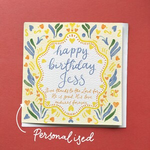 May include: A cream-coloured birthday card with a decorative border of blue, yellow, and orange floral elements. The card features the text "happy birthday Jess" in blue script, with additional text below. The word "Personalised" is written at the bottom of the card.