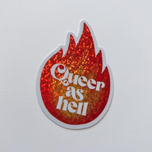 Peut inclure: Un autocollant en forme de flamme avec un motif rouge et orange pailleté. Les mots "Queer as hell" sont écrits en blanc, en lettres stylisées, au centre de la flamme.