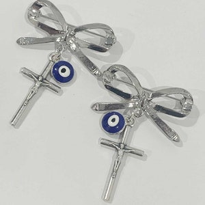 May include: Two silver bow brooches with a blue evil eye charm and a silver crucifix pendant.