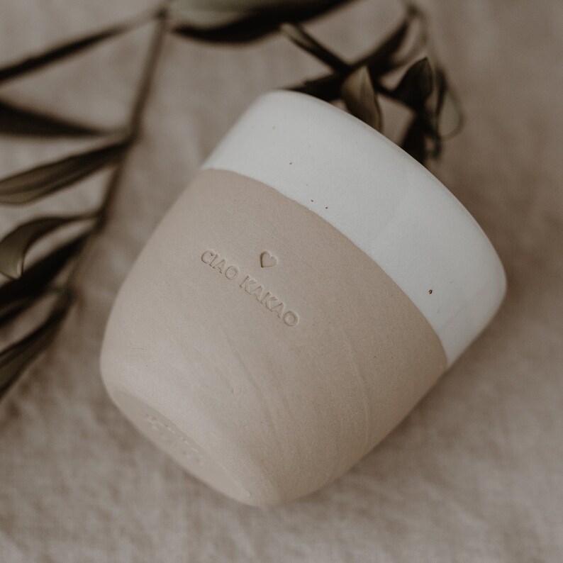 May include: A white and beige ceramic mug with the text 'CIAO KAKAO' and a heart symbol on the side.