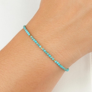 May include: A delicate turquoise beaded bracelet with small gold accents. The bracelet is worn on a wrist against a white background. The beads are a vibrant turquoise colour.