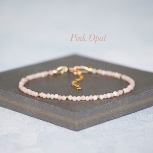 Puede incluir: Una pulsera delicada con peque&ntilde;as cuentas de &oacute;palo rosa facetadas intercaladas con diminutos espaciadores de metal dorado. La pieza de joyer&iacute;a incluye una cadena extensora de metal dorado y un cierre de mosquet&oacute;n. El texto Pink Opal es visible.