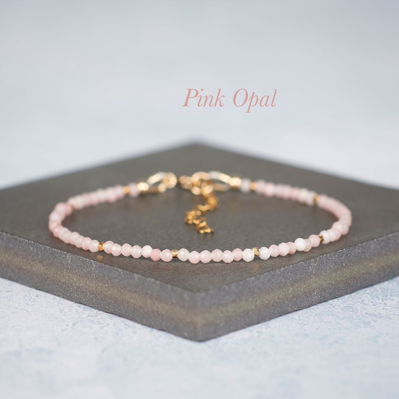 Puede incluir: Una pulsera delicada con peque&ntilde;as cuentas de &oacute;palo rosa facetadas intercaladas con diminutos espaciadores de metal dorado. La pieza de joyer&iacute;a incluye una cadena extensora de metal dorado y un cierre de mosquet&oacute;n. El texto Pink Opal es visible.
