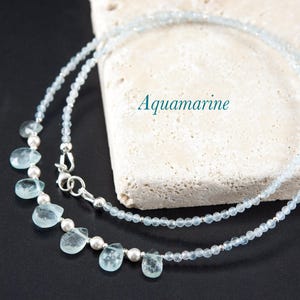 May include: A delicate silver necklace with a double strand of light blue aquamarine beads. The necklace features a row of larger aquamarine teardrop-shaped stones.