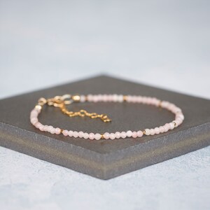 Puede incluir: Una pulsera delicada con peque&ntilde;as cuentas facetadas de color rosa p&aacute;lido dispuestas en un patr&oacute;n circular continuo. El dise&ntilde;o est&aacute; acentuado con diminutos espaciadores de metal dorado reflectante e incluye una cadena extensora dorada.