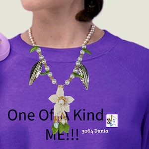 May include: A handcrafted necklace with a white flower pendant, pearl accents, and green bead dangles. The necklace incorporates faux pearls, gold-tone beads, and silver-tone leaf charms. The text "One Of A Kind ME!!!" is visible.