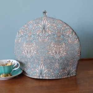 Könnte beinhalten: Eine blaue und cremefarbene Teekanne mit einem floralen Muster. Die Teekanne ist aus Stoff und hat einen Griff oben.