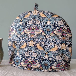 May include: A blue tea cosy with a floral pattern featuring birds and berries. The pattern is reminiscent of William Morris designs.