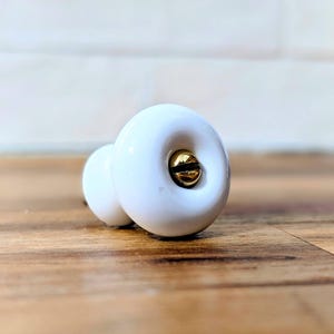 May include: A white ceramic mug with a black handle and the text "But First, Coffee" in a black, handwritten-style font. The mug is on a white surface.