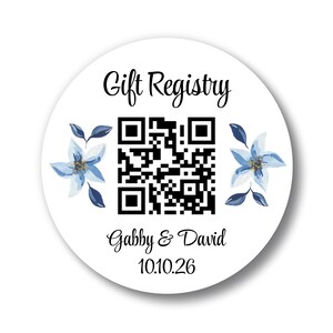 May include: A white round sticker with the text "Gift Registry" in black script. It features a QR code, blue floral accents, and the names "Gabby & David" with the date "10.10.26" in black script.