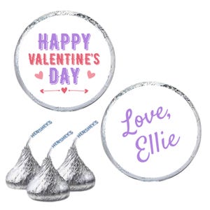 May include: Hershey's Kisses candies with silver foil wrappers. Two circular stickers read "Happy Valentine's Day" and "Love, Ellie" in purple and pink lettering. The image is on a white background.
