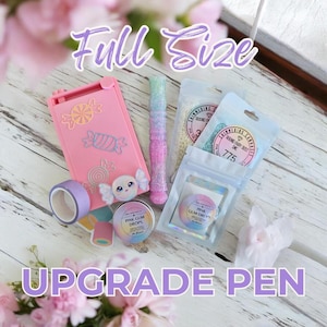 Puede incluir: Una colección de materiales de manualidades, que incluye un bolígrafo rosa, purpurina rosa y blanca y pequeñas bolsas de adornos. La imagen también presenta una funda rosa con pegatinas con temática de caramelos y el texto "Full Size" y "Upgrade Pen".
