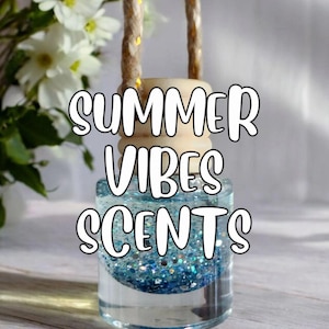 May include: A clear glass air freshener with blue glitter and the words "SUMMER VIBES SCENTS" in white. The air freshener has a wooden top and a rope for hanging. White flowers are in the background.