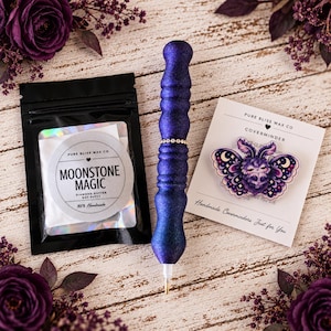 Op de afbeelding: Een donkerblauwe glitterende diamant schilderpen met een strass band, een zwart zakje met het label Moonstone Magic Diamond Dotter Dot Putty, en een witte kaart met een paarse mot illustratie van Pure Bliss Wax Co.