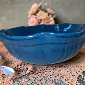 May include: A deep blue ceramic bowl with a scalloped, wavy rim and a smooth, glossy finish. The bowl features a rounded, wide basin with subtle vertical indentations along the exterior walls, creating a textured appearance in the glaze.
