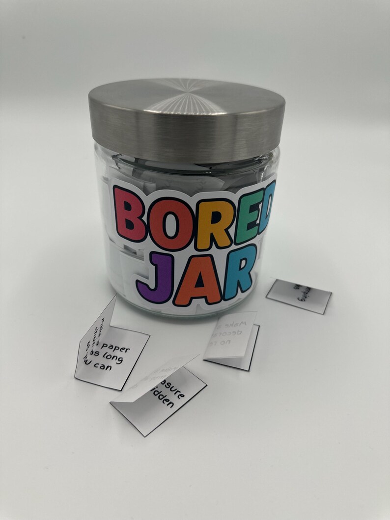 May include: A glass jar with a silver lid, labelled "BORED JAR" in colourful letters. Small folded white papers with handwritten text are scattered around the jar. The jar is filled with similar folded papers.