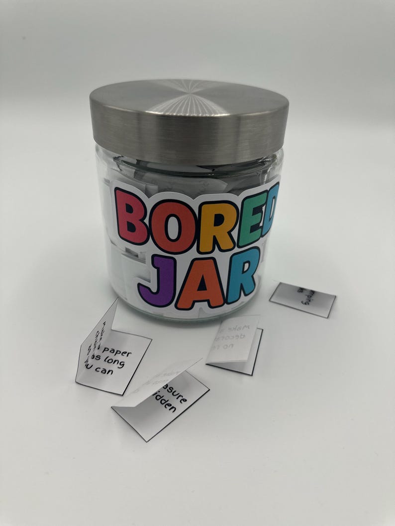 May include: A glass jar with a silver lid, labelled "BORED JAR" in colourful letters. Small folded white papers with handwritten text are scattered around the jar. The jar is filled with similar folded papers.