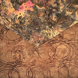 May include: A brown fabric pouch with a flap closure. The flap is made of a different fabric with a floral pattern in shades of brown, yellow, and pink. The pouch has a circular pattern in shades of brown.