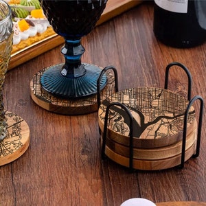 May include: Set of four wooden coasters with a black and white city map design. The coasters are stacked and held together by a black metal frame.