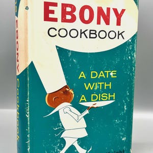 Może przedstawiać: Książka kucharska w stylu vintage zatytułowana "The Ebony Cookbook" z turkusową okładką. Na okładce znajduje się rysunkowy szef kuchni i tekst "A Date With A Dish". Książka jest autorstwa Fredy DeKnight.