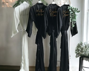 Long black personalized satin bridesmaid robes with front and back gold text. Custom gifts for Mother of the Bride, Groom and Bridal party.