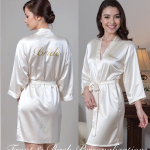 A personalized white satin robe featuring gold K on the front and Bride on the back. Text highlights customization options for front, back, or no text. Set in a lush outdoor environment, perfect for weddings or special occasions.