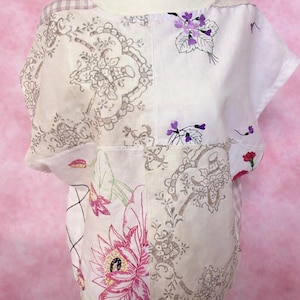 May include: A patchwork top with a scoop neck and short sleeves. The top features floral and patterned fabric panels in white, grey, and pink. Embroidered flowers and botanical designs add detail to the garment.