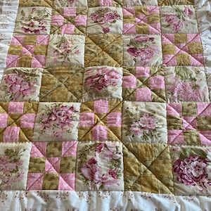May include: A patchwork quilt featuring a floral design in shades of pink, green and brown. The quilt is made up of squares and rectangles, and the fabric is quilted with a diamond pattern.
