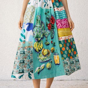 May include: A midi-length patchwork skirt featuring a variety of colourful fabric panels. The central panel displays a vibrant illustration of a green glass bottle, a cocktail glass, red flowers, yellow bananas, a bowl of fruit, and a glass of orange juice.