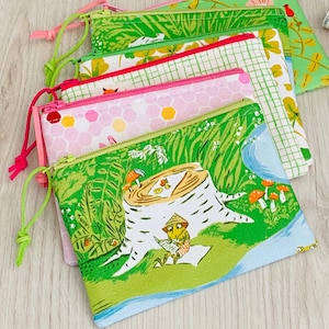 Peut inclure: Plusieurs pochettes zippées colorées avec divers motifs, notamment floraux, géométriques et des scènes de forêt. Chaque pochette a une fermeture éclair de couleur différente et un cordon assorti. Les pochettes sont en tissu.