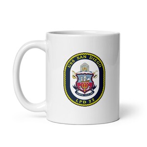 May include: White ceramic coffee mug with a navy blue and gold crest featuring the text "USS SAN DIEGO LPD 22" and the words "SEMPER VIGILANS".