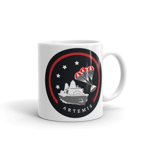 Könnte beinhalten: Weiße Keramiktasse mit einem schwarzen und roten kreisförmigen Design, das ein Raumschiff mit einem Fallschirm und dem Wort "ARTEMIS" zeigt.