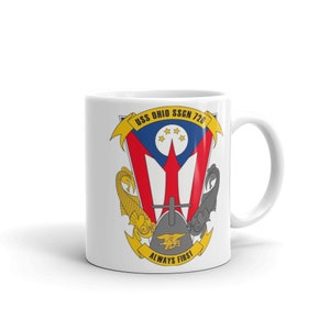 Puede incluir: Taza de cerámica blanca con una imagen colorida del escudo de armas del USS Ohio SSGN 726. El escudo presenta una bandera roja y blanca con una estrella azul y un tridente dorado. El texto "USS OHIO SSGN 726" y "ALWAYS FIRST" está impreso en amarillo.