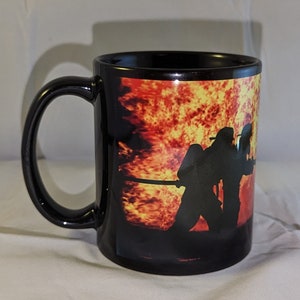 May include: Black ceramic coffee mug with a graphic of firefighters silhouetted against a fiery orange and yellow background.