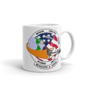 May include: White ceramic mug with a colorful graphic of the Space Shuttle Challenger crew patch. The patch features a stylized American flag, a globe, and a space shuttle. The names of the crew members are listed around the edge of the patch: Mcnair, Onizuka, Resnik, Scobee, Smith, McAuliffe, and Jarvis.
