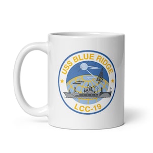 Op de afbeelding: Witte keramische mok met een blauwe en gele afbeelding van het insigne van de USS Blue Ridge LCC-19. Het insigne toont een schip, een wereldbol en een satellietschotel.