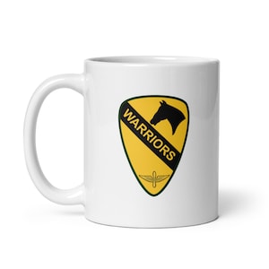 May include: White ceramic mug with a yellow and black military insignia featuring a horse's head and the word "WARRIORS".