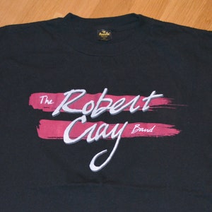 Puede incluir: Camiseta negra con un estampado gráfico rojo y blanco de "The Robert Cray Band".